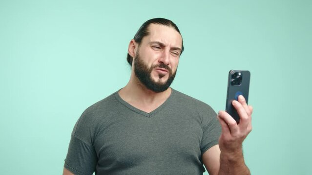 A man with a tied-up ponytail and black beard displays intensity during a video call, his stern expression and assertive speech indicating a serious discussion against a turquoise backdrop. Camera 8K