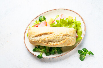 Ciabatta sandwich with lettuce, cheese, tomatoes and ham on white table.