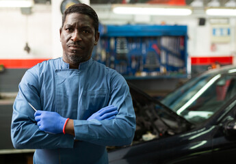 Portrait of afro american auto mechanic man standing near car in auto workshop