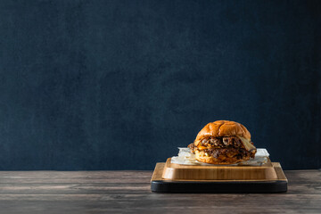 Deliciosa hamburguesa con doble carne aplastada, doble queso sobre tabla de cocina en una mesa de madera rústica en un fondo azul - obrazy, fototapety, plakaty