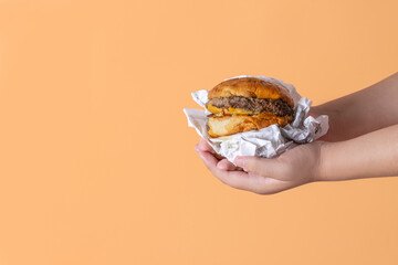 Manos de niña sosteniendo una hamburguesa con fondo naranja en vertical para redes sociales