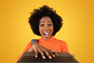 Excited young woman with an afro hairstyle exuberantly typing on a laptop