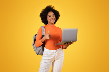 Cheerful young woman with an afro gives a thumbs-up while holding a laptop