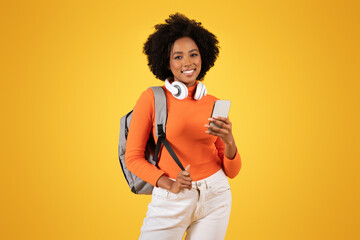 Confident young woman with curly afro hair and headphones around her neck checks her smartphone
