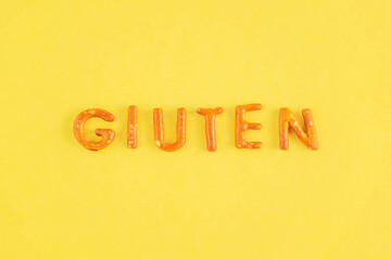 The word gluten is laid out in cookie letters on a yellow background. Gluten food concept.
