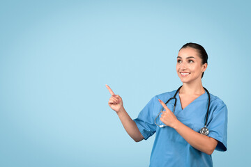 Confident woman nurse in blue scrubs pointing upwards at blank space