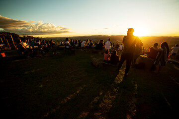 Silhueta de pessoas assistindo o por do sol no alto de uma serra. 