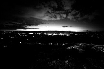 Paisagem em preto e branco de cidade e céu carregado de nuvens durante a noite. 