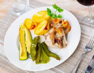 Appetizing pieces of baked rabbit with potatoes and vegetables. Decorated with a sprig of fresh...