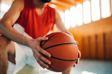 Fotobehang Close up of basketball player's hands holding a ball on court. © Zamrznuti tonovi
