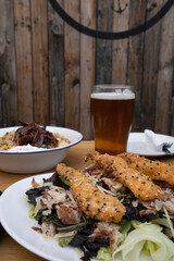 Caesar salad and a beer. Close up view of fresh a salad with lettuce, parmesan cheese, bread croutons, fried chicken fingers breaded with sesame seeds and crispy bacon.