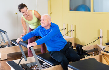 Elderly man doing exercise with her personal trainer in pilates studio