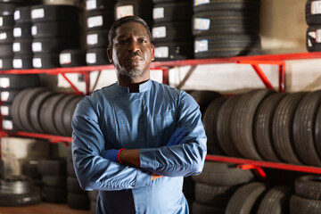 Portrait of a serious auto mechanic in front of car tires