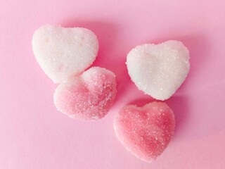 Obraz premium a group of pink and white heart-shaped chewy candies on a pink background. chewy candy sprinkled with granulated sugar. sweet and chewy 