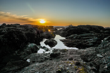 Sunset above rocks and tide pools on the Oregon Coast in Lincoln City at Roads End.   Glistening water, rock formations and soft sunshine.