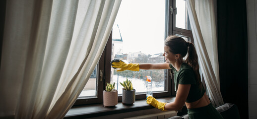 Weekend homework. Young pretty woman washes window in cozy living room at home.