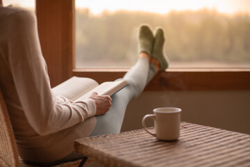 Woman Person relaxing at home reading book feeling relaxed on a cozy winter morning enjoying cup of hot tea coffee
