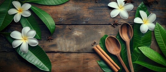 A wooden table is adorned with white flowers and wooden spoons. The green plant with frangipani cinnamon adds a touch of nature to the aged wood surface.