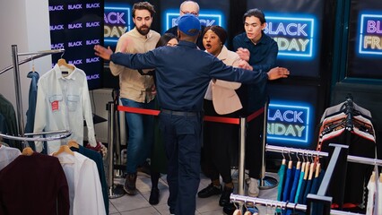 Fototapeta na wymiar Anxious clients push guard at store to enter mall for black friday discounts and deals, standing behind red tape at entrance. Diverse crazy people being aggressive to open shopping center.