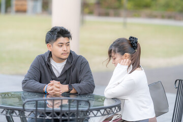 A young Japanese male and female couple in their 20s discussing in a green park in Nagoya City,...