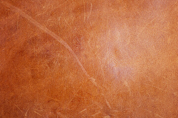 A piece of brown genuine leather with scratches. Leather background macro photo.
