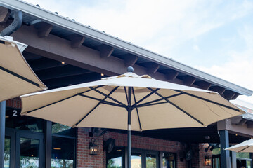 Multiple large summer nylon patio shade umbrellas, beige colored, opened with brown wooden...