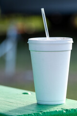 A large white nonrecyclable to-go drink cup with a plastic lid and straw on a vibrant green patio...