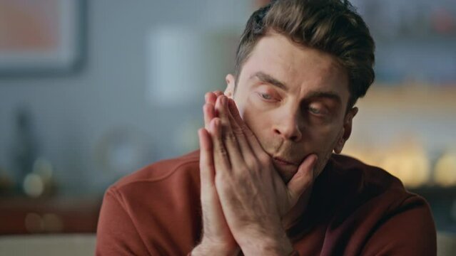Pensive man sitting home in living room close up. Portrait serious guy thinking