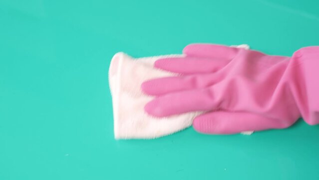 Female hand in pink glove wipes mint surface with rag.