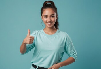 Young woman in a casual teal top giving a thumbs up, her poised smile suggesting approachability and warmth. - obrazy, fototapety, plakaty