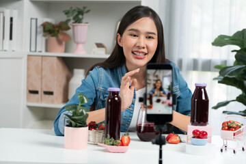 Smiling young beautiful Asian reviewing tasty mixed strawberry and cherry juice detox drinks,...