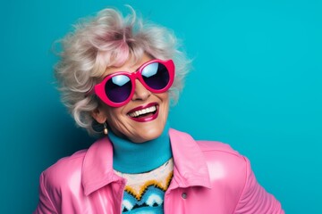 Fashionable senior woman in pink clothes and sunglasses on blue background