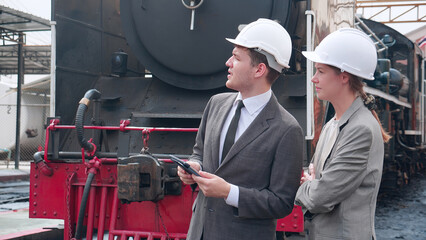 Young caucasian engineer man and woman in suit checking train with tablet in station, team engineer inspect system transport, technician examining infrastructure, transportation and industry.