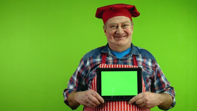 Senior chef in red apron showing tablet with blank advertising display.