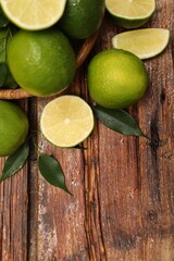 Fresh limes and green leaves with water drops on wooden table, flat lay. Space for text