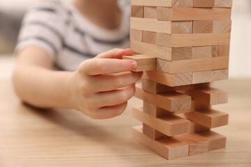 Child playing Jenga at wooden table indoors, closeup