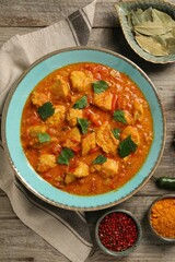 Delicious chicken curry and ingredients on wooden table, flat lay