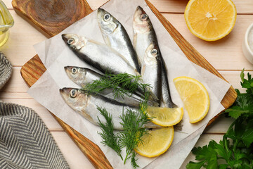 Fresh raw sprats, lemon and dill on light wooden table, flat lay