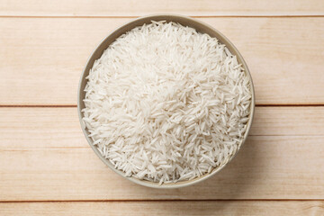 Fototapeta na wymiar Raw basmati rice in bowl on white wooden table, top view