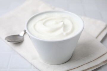 Obraz na płótnie Canvas Delicious natural yogurt in bowl and spoon on white table, closeup