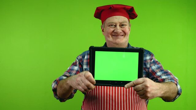 Senior chef in red apron showing tablet with blank advertising display.