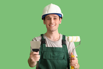Male worker with putty knife and paint roller on green background