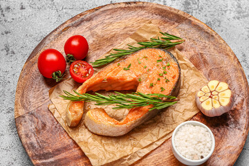 Plate of tasty salmon steak with tomatoes and garlic on grey background