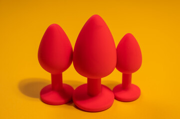 Three size silicone red butt plugs on an orange background.