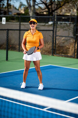 A woman in an orange outfit plays pickleball on a blue court