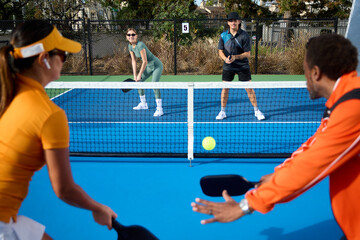 A young couple is waiting to defend on a pickleball court from across the net