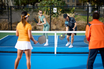 A mixed group of pickleball players plays on a blue court during the day