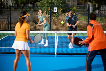 A mixed group of pickleball players plays on a blue court during the day