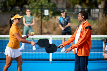 A mixed group of pickleball players plays on a blue court during the day