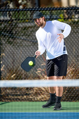 A man in a white shirt plays a game of pickleball in the fall